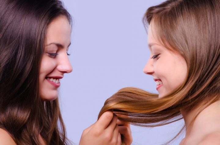 Two smiling girls playing with their beautiful long hairs.