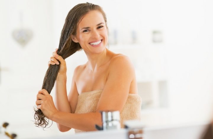 Happy young woman applying hair mask in bathroom
